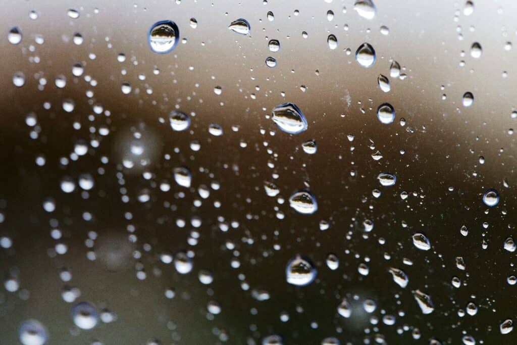 raindrops on a greenhouse glass surface with a blurred brown background